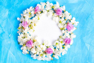 Mavi arkaplanda beyaz ve pembe akasya çiçeklerinden yapılmış boş çiçek çemberi çerçevesi..