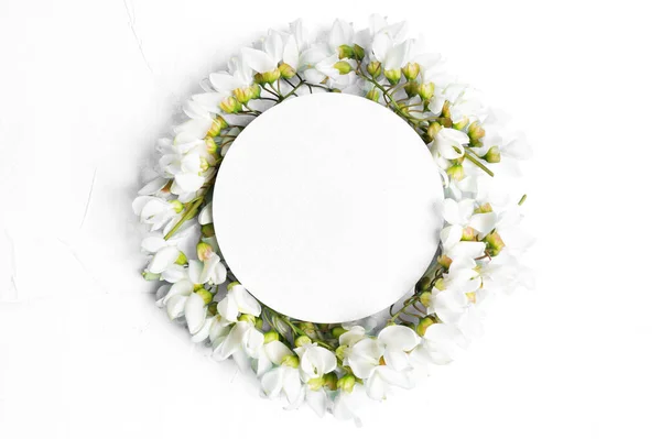 Circle floral frame arranged from white acacia flowers on white background with copy space. Invitation card template.
