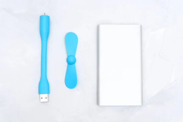 Portable usb fan and a slim silver power bank isolated on a neutral background. Mobile cooling technology.