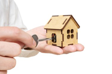 Adam evin anahtarını beyaza izole edilmiş minyatür bir oyuncak evin içine yerleştiriyor. Daire kiralama konsepti.
