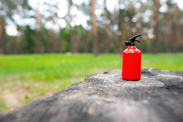Miniature fire extinguisher placed on a burnt tree stump against a forest background. Wildfire prevention concept.