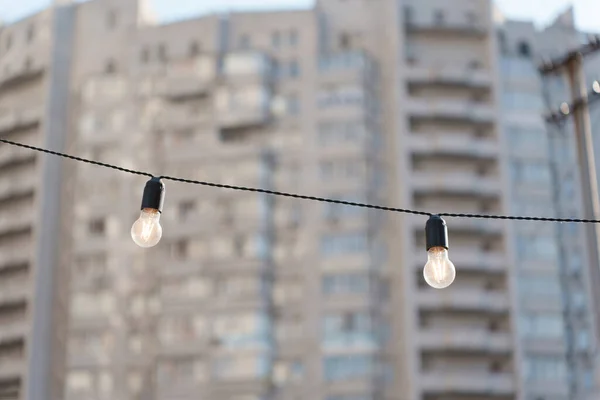 Two glowing light bulbs on a wire with a residential building background. Street lighting modernization concept.