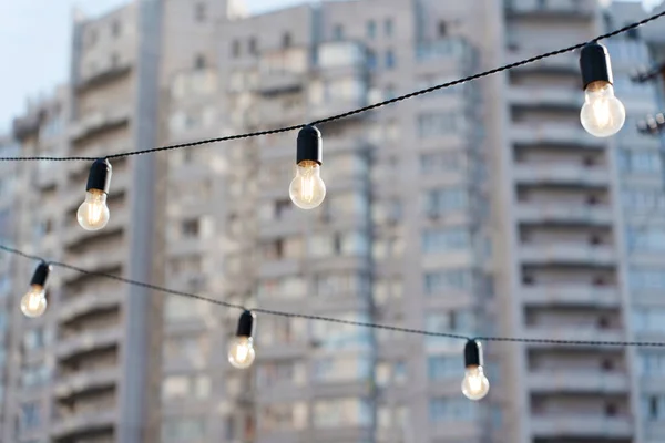 Group of glowing light bulbs on wires with a residential building background