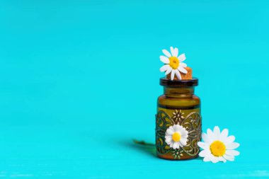 Kırmızı papatya yağı ve açık mavi arka planda papatya çiçekleri olan küçük bir şarap şişesinin yakın çekimi..