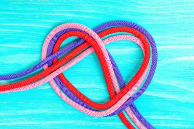 Mavi ahşap arka planda bükülmüş üç renkli ipten yapılmış kalp sembolü. Yaratıcı ilişki kavramı.