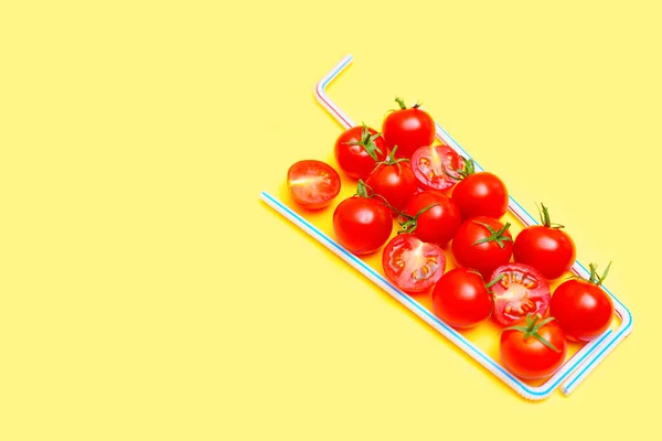 Refreshing tomato cocktail recipe concept. Whole and halved ripe cherry tomatoes framed with drinking straws on a vibrant yellow background.