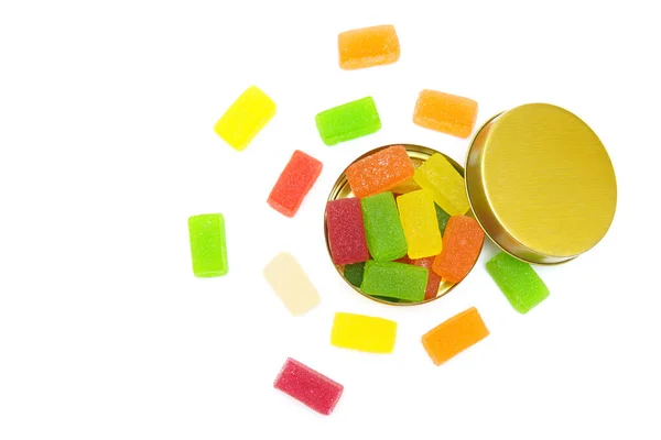 Candy box with mixed fruit jelly cubes scattered on white background, top-view.