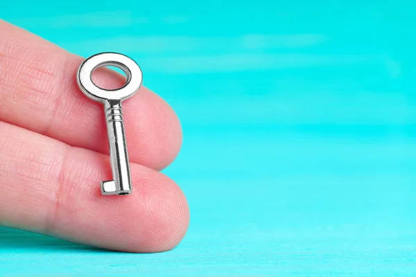 Small silver-toned skeleton key in hand against blue background with copy space. Solution offering concept.