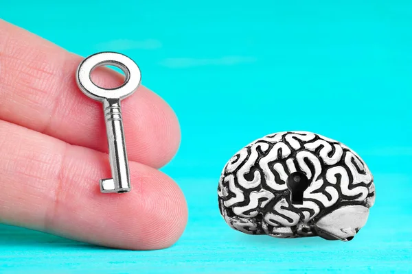Anatomical copy of a human brain having a keyhole and a small master key in hand isolated on blue background. Unlock secrete power of the brain.