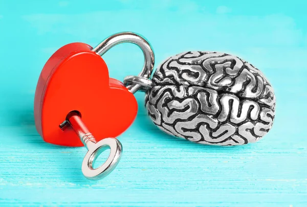 Anatomical copy of a human brain attached to a red heart-shaped padlock with a key isolated on blue wooden background. Brain affections control concept.