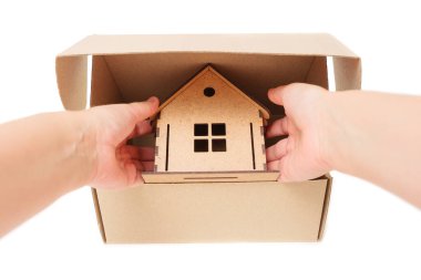 Hand taking a wooden toy house out of a cardboard box isolated on white. Buying a dream home.