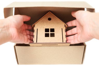 Hand taking a wooden toy house out of a shipping box on white. Creative relocation concept.