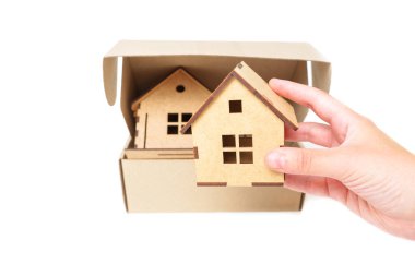 Hand packing toy houses inside a shipping box on white. Creative relocation concept.