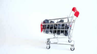 Fresh blueberry falling into a miniature shopping trolley isolated on white