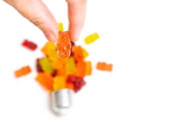 Pinch holding an orange gummy bear candy over a lightbulb shape isolated on white background, focus on foreground.