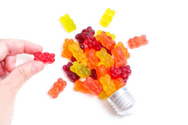 Hand arranges a lightbulb shape using multicolored gummy bear candies and a cap. Sweet food affecting creativity.