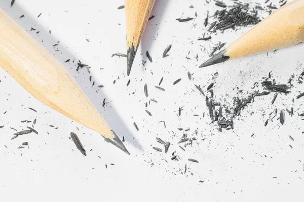 Three sharpened pencils with lead shavings on white background.