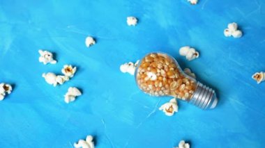Lightbulb full of popcorn kernels on a blue background. Popped corns falling on the table.