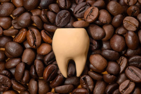 Large coffee stained tooth on a pile of roasted coffee beans. Creative teeth whitening concept.