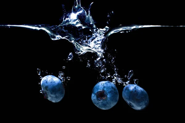 Fresh ripe blueberries dropped underwater with air bubbles and splashes isolated on black background.