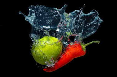 Hot red chilli and fresh whole lime dropped underwater with splashes isolated on black background.