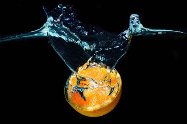 Juicy orange half falling underwater isolated on black background