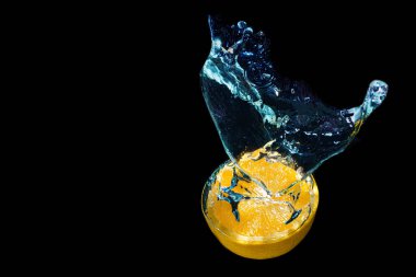 Fresh halved citrus fruit dropped in water with splashes on black background