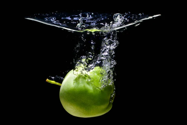 Green apple going underwater with splashes and bubbles on black background.