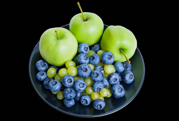 Apples, blueberries and grapes on a black plate isolated on black background. Healthy dessert concept.