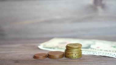 Throwing some dollar bills on the table and putting a miniature house model on a coins stack placed on a wooden background.