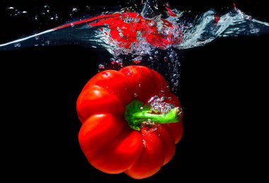 Large orange bell pepper dropped in water with splashes isolated on black background.