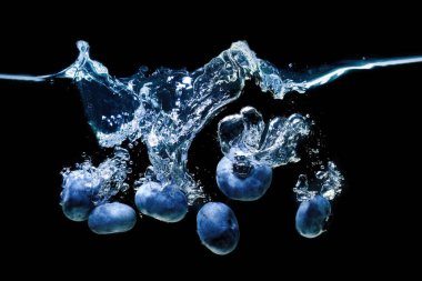 Bunch of fresh blueberries dropped in water with air bubbles and splashes isolated on black background.