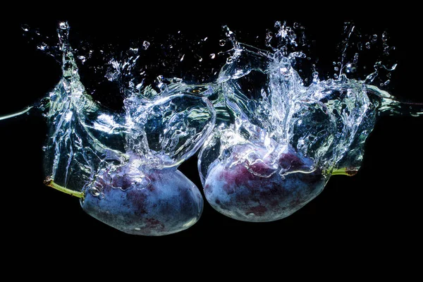 Two damson plums dropped in water with splashes isolated on black background.