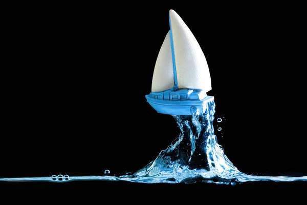 Blue toy sailboat figurine rises on a wave isolated on black background. Catching the next wave in business.