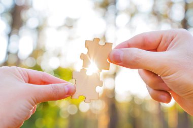 Ellerin tahtadan yapboz yapbozları ile güneş ışığının geldiği Bokeh ormanının arka planındaki yapbozları eşleştirmeye çalışırken görüntüsü. Yaratıcı ruh eşi konsepti.
