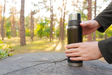 Siyah termos şişesi erkeklerin elinde orman geçmişi olan büyük bir ağaç kütüğünün üzerinde. Ormanda kahve molası veriyoruz..