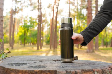 Erkek el, ormandaki büyük bir ağaç kütüğüne siyah bir termos şişesi koyar..