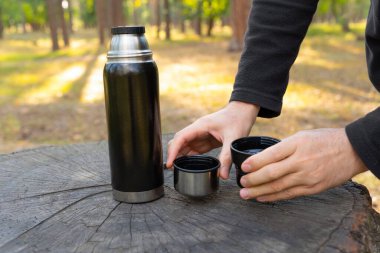 Annem bir termos şişesinin iki bardağını ormandaki büyük bir ağaç kütüğüne koyar. Ormanda güneşli bir günde kahve molası..