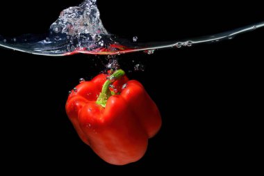 Büyük kırmızı bir biberin yakın plan çekimi suya düşer ve siyah üzerine su sıçrar..