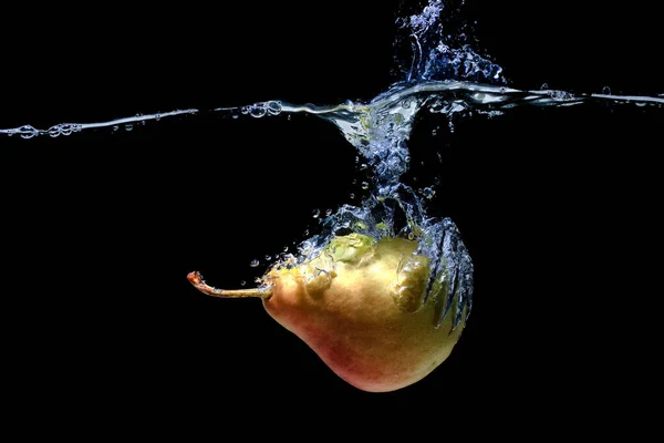 Fresh whole pear dropped in water with splashes isolated on black background.