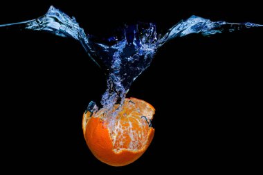 Soyulmuş bir mandalinanın yakın plan görüntüsü, kara zemine izole edilmiş sıçramalarla birlikte su altına düşmesi..