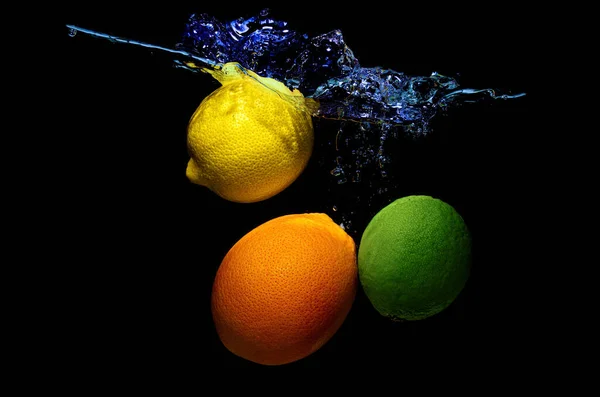 Mix of citrus fruits dropped in water with splashes isolated on black background.