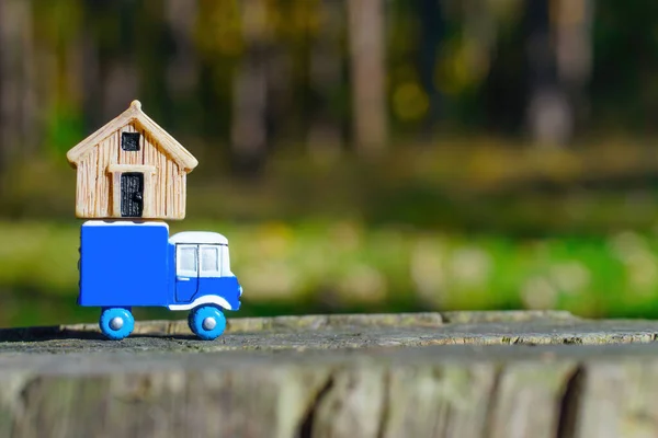 Small box truck carrying a tiny house on top placed on a tree stump in the woods. Selective focus, copy space. Countryside relocation.