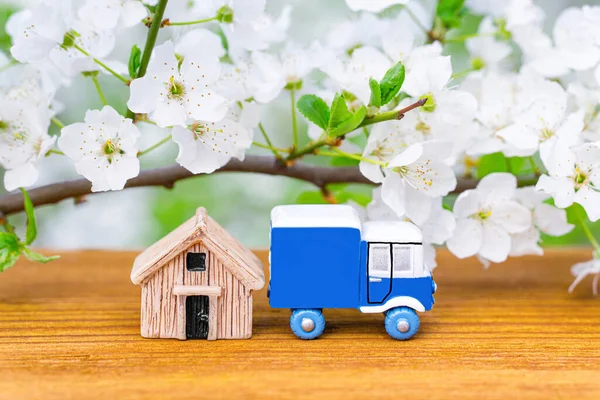 Toy truck and small wooden house against a blooming tree background. Spring season home purchase and relocation concept.