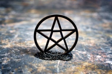 Dağınık bir arka plana yerleştirilmiş siyah bir pentagram kolyesinin yakın çekimi.
