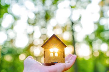 Elinde yeni yapılmış küçük ahşap bir ev. Penceresinden güneş ışınları gelen odakları kesilmiş doğal bir arka plan..