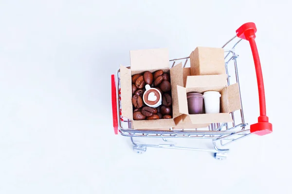 Small shipping boxes full of roasted coffee beans and paper coffee cups in a miniature push cart isolated on white background with copy space, top view.