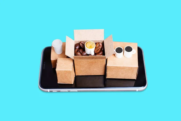 Coffee supplies e-commerce set-up: tiny cardboard boxes with roasted coffee beans and coffee cups placed on a smartphone isolated on blue.