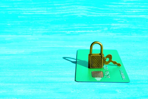 Bronze-toned padlock with key placed on a green credit card isolated on a blue background with copy space. Fraud security and protection concept.