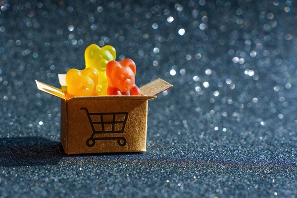 Three colorful gummy bear candies in a tiny shipping box labeled with a shopping cart symbol.